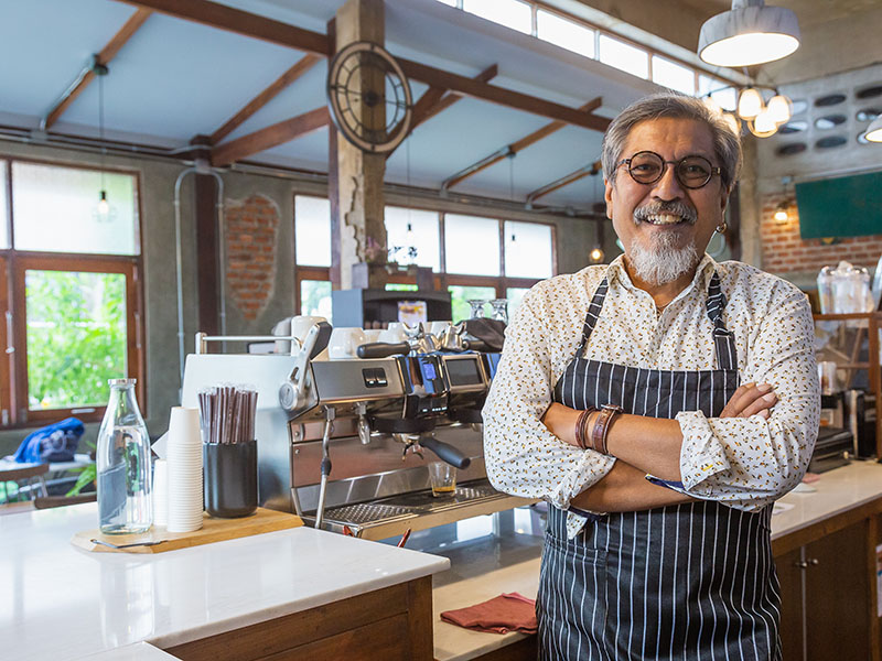 Portrait of Asian senior man Barista or coffee owner using coffee machine and looking to camera at bar counter in coffee shop cafe, Small business owner concept