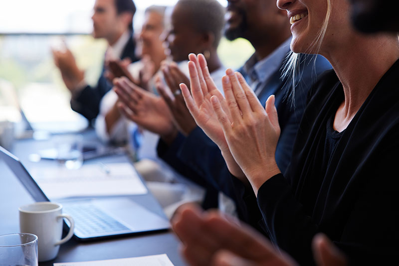 Diverse businesspeople sitting together at a boardroom table and clapping