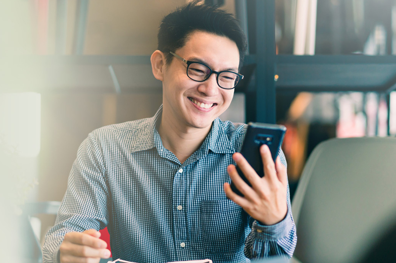 A man with glasses looks at his cellphone and smiles