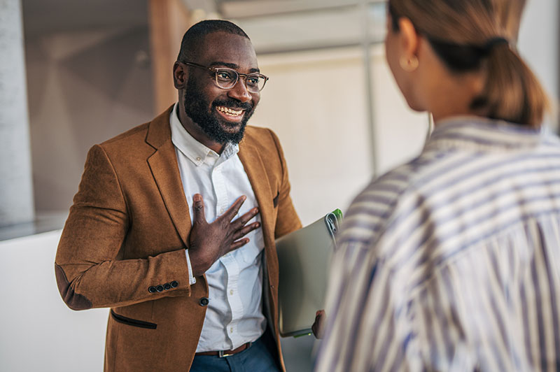 A man with glasses rests his hand on his heart as he speaks to a woman