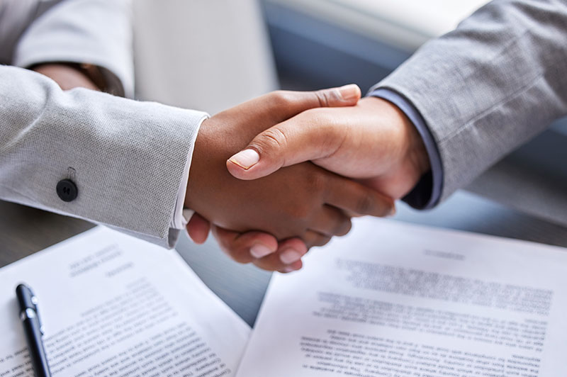 Two people shakes hands over a pile of papers