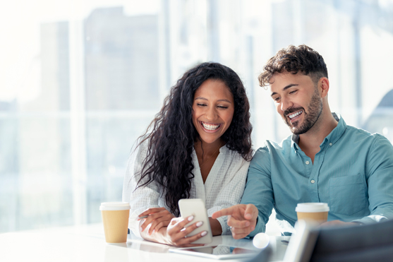 A man points and laughs at something on a coworkers phone