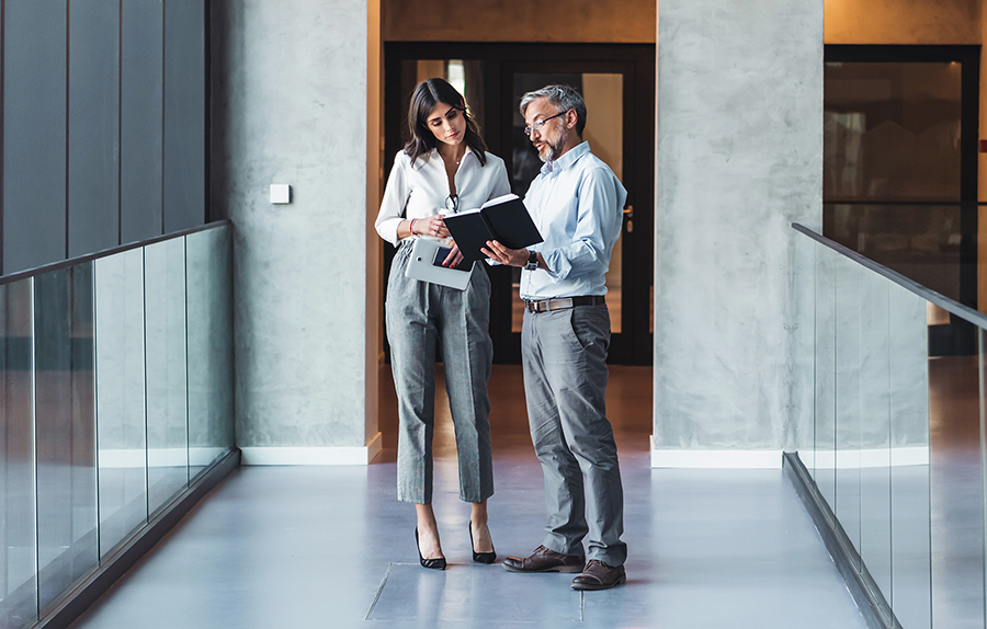 Two business people reviewing text while standing in an office hallway