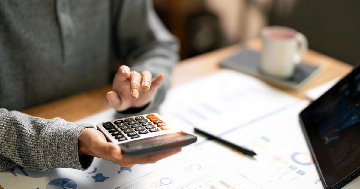 A person types on their large calculator with their coffee