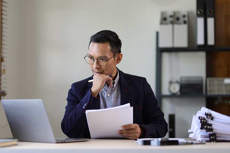A man with glasses rests his hand on his chin as he thinks deeply
