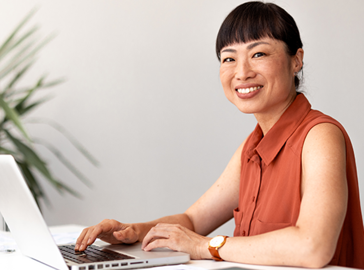 A woman with short hair types at her laptop and looks into the camera