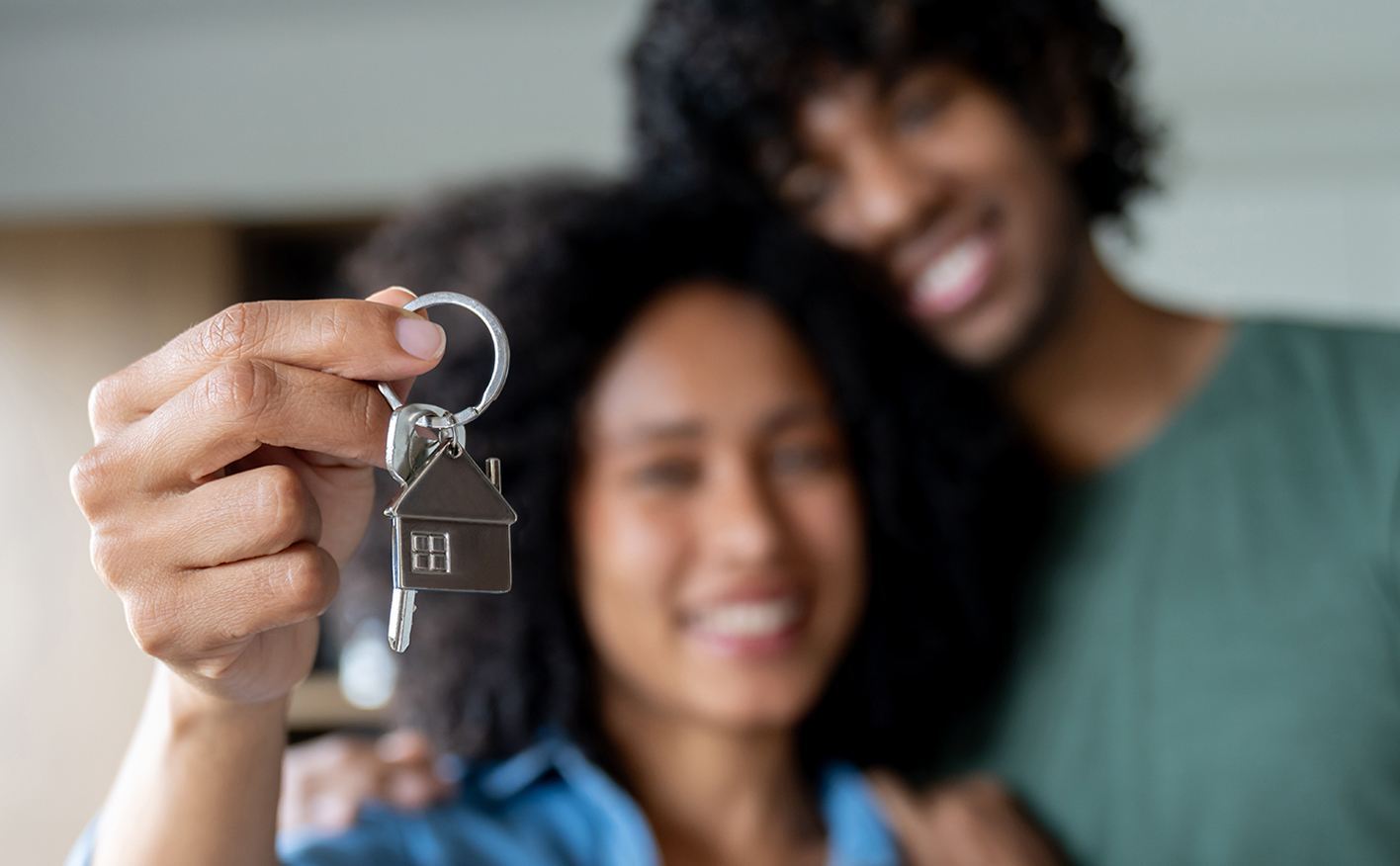 A out-of-focus young couple hold their house keys to the camera