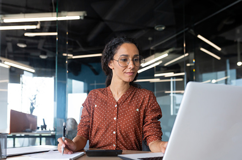 A woman with glasses works at her laptop while in the office