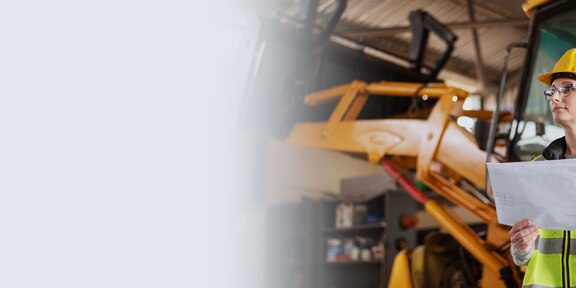 Construction working in front of equipment, holding plans