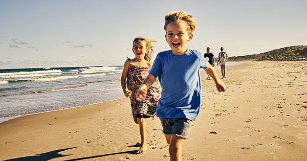 Two children are running down the beach in front of his parents