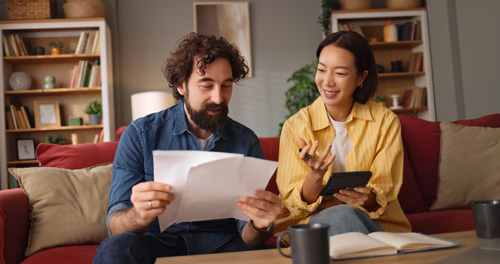 A man with a beard looks at documents while a woman in a yellow shirt types on a calculator